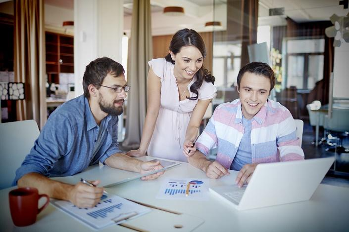 A group of people sitting at a table looking at a computer 
Description automatically generated with medium confidence